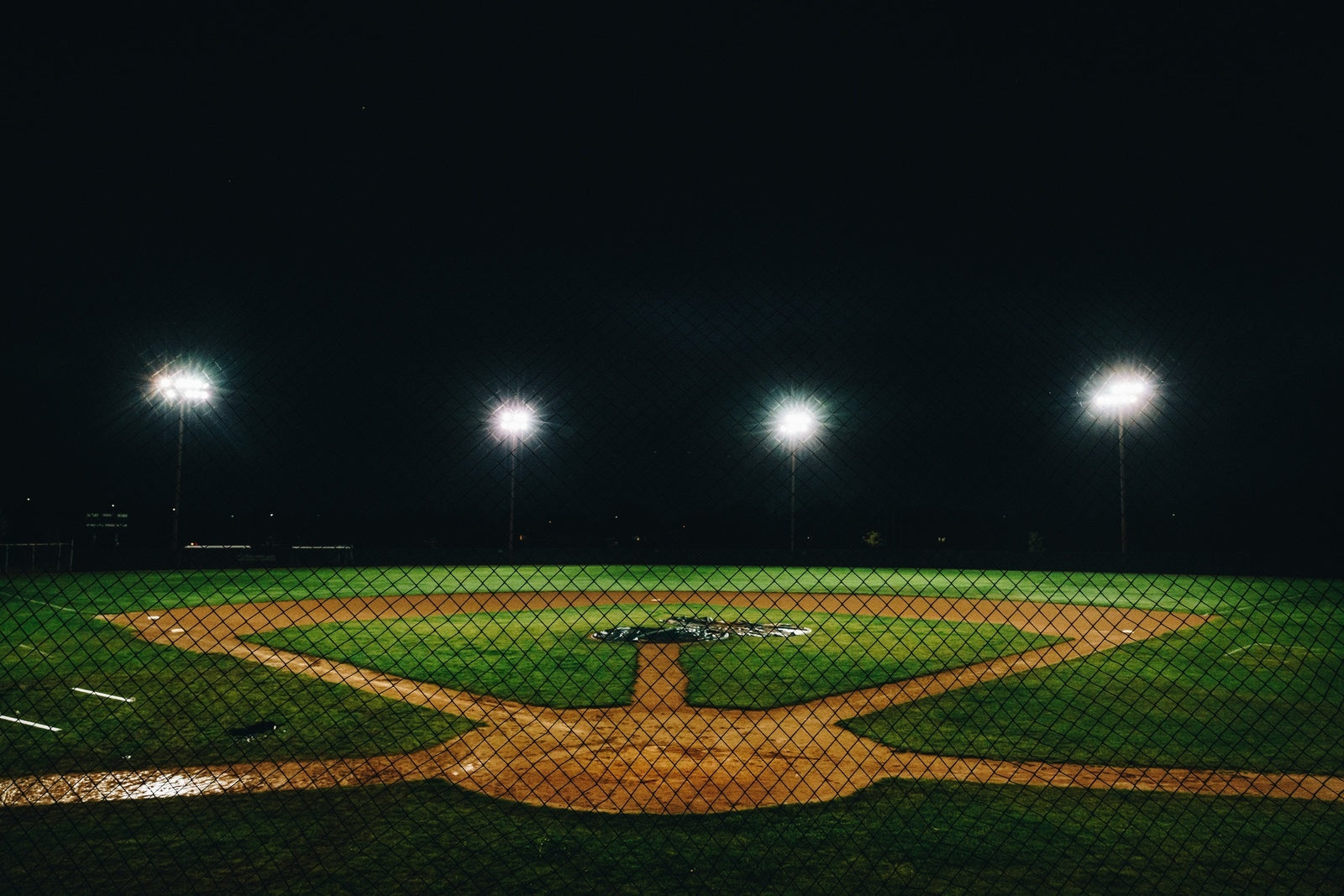 Empty Baseball Field, with lights on in the background shining onto the green grass and infield dirt.